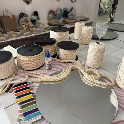 Mesa de taller con rollos de cordón de algodón, un espejo, y una paleta de hilos, materiales textiles de Interhilos para manualidades.