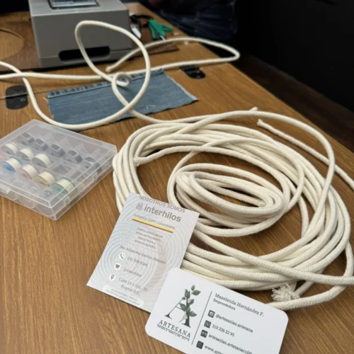 Mesa de taller interhilos con un cordón de algodón blanco y una tarjeta de presentación de Interhilos junto a una máquina de coser.