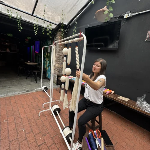 Talleres interhilos en su taller de embarrilado Bogotá con participante trabajando en técnica textil con hilos y cuerdas sobre estructura metálica en espacio interior.